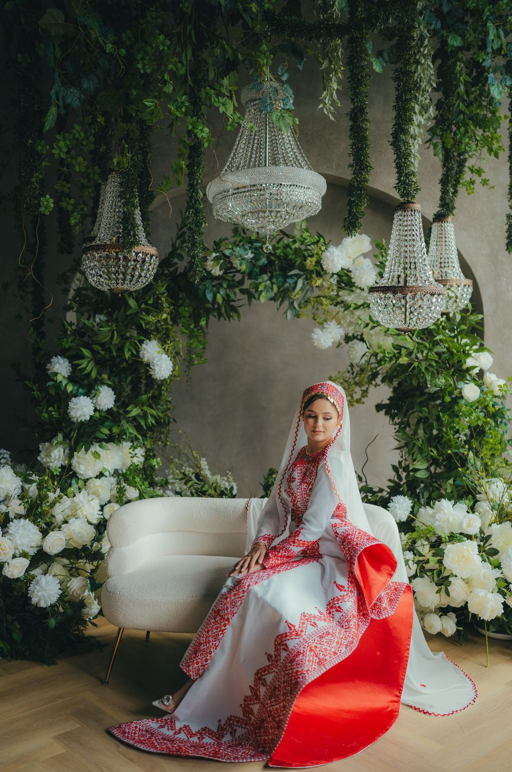 Elegant wedding setting with crystal chandeliers, white floral arrangements, and a bride in traditional red and white attire.