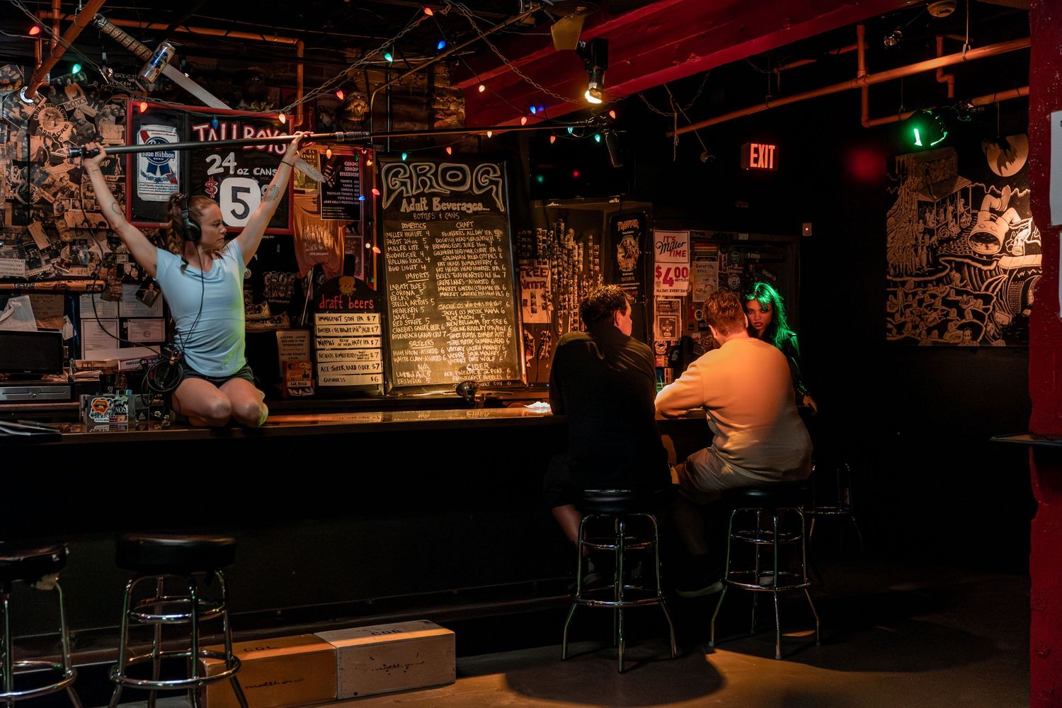 Bar patron celebrates energetically at counter while others sit nearby in dark pub setting.