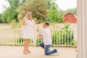 A proposal moment captured on wooden deck with red barn in background during golden hour.