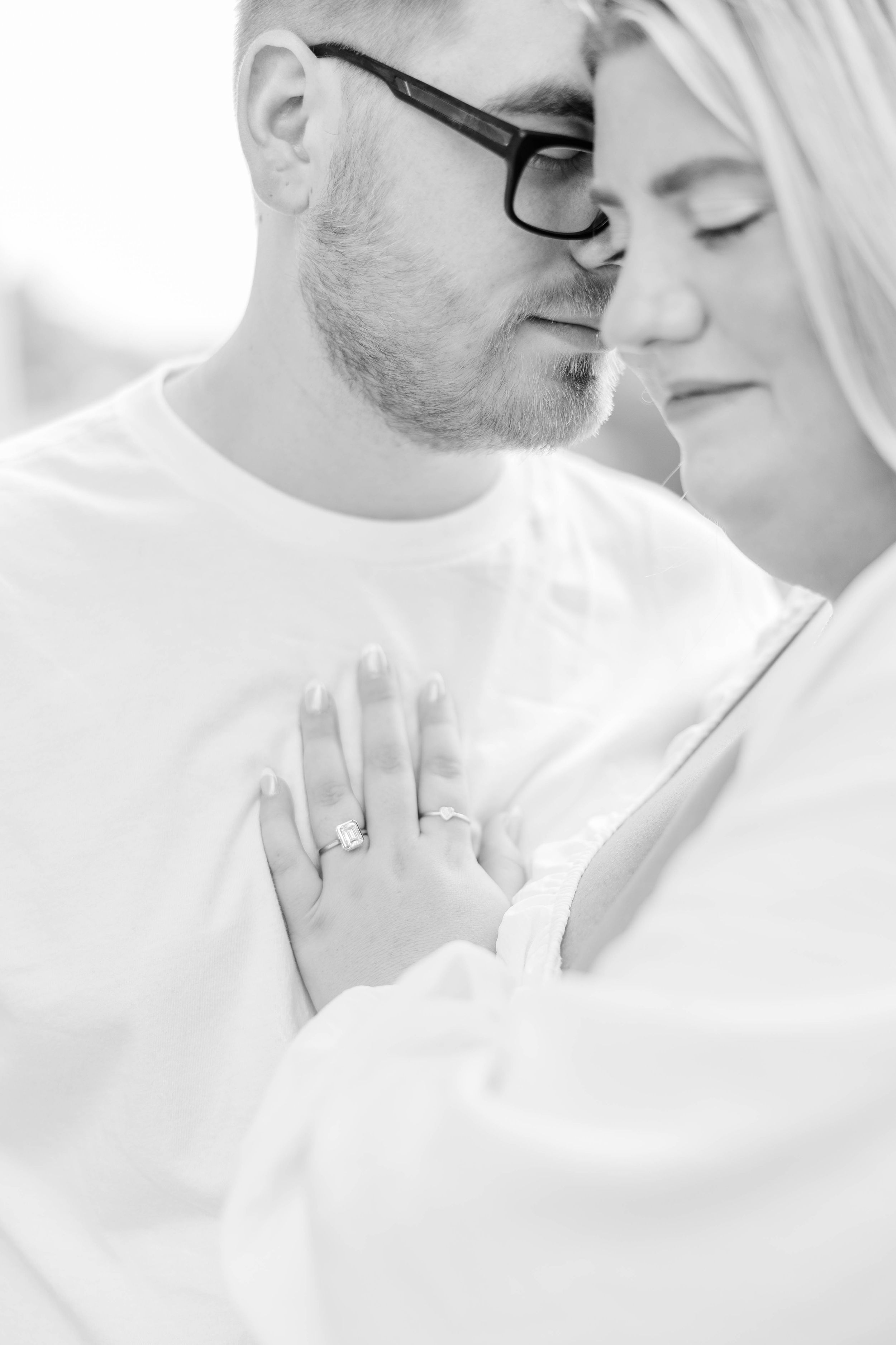 Intimate couple embraces in romantic black and white portrait series against white background.