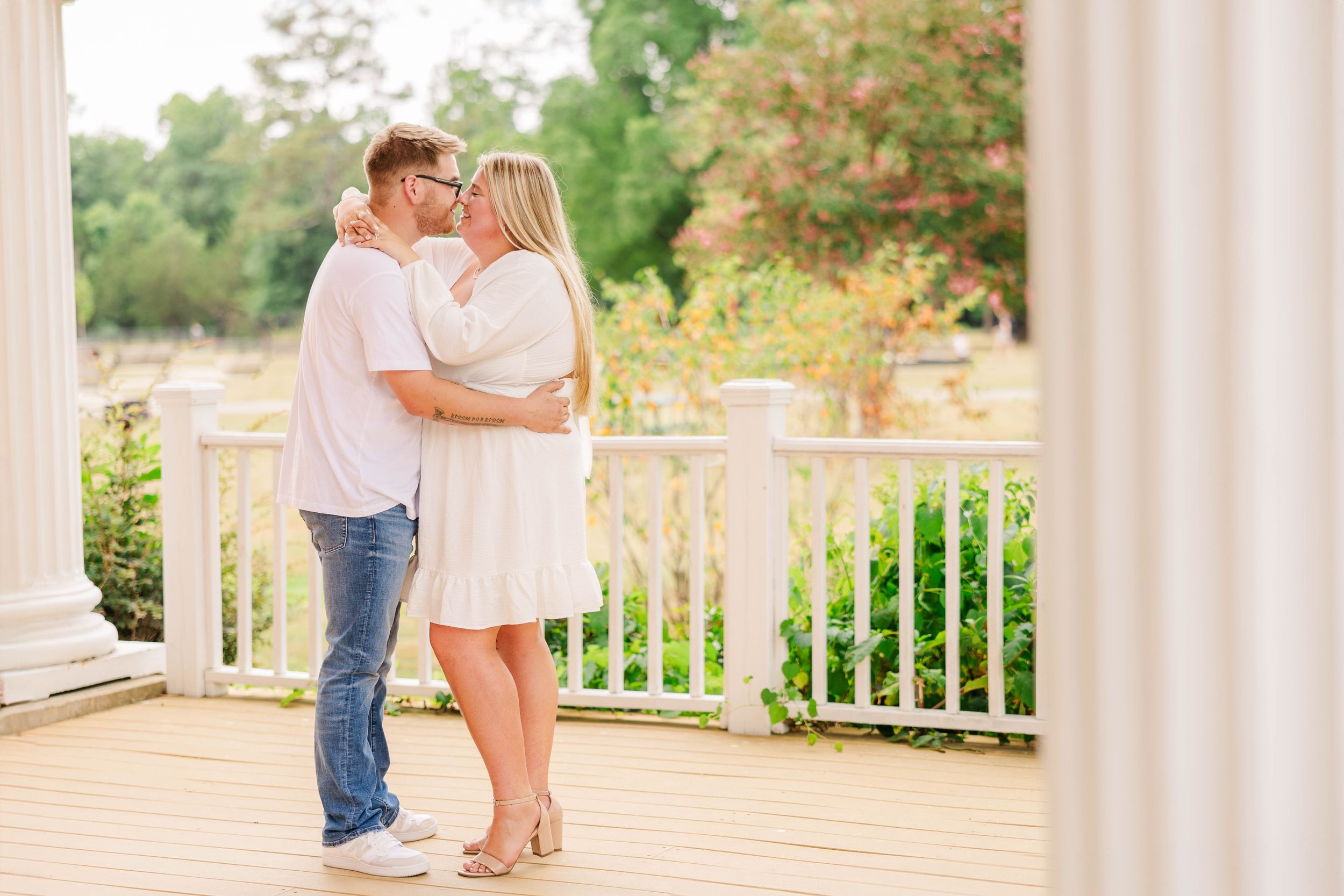Romantic outdoor photoshoot with white columns and greenery in background.