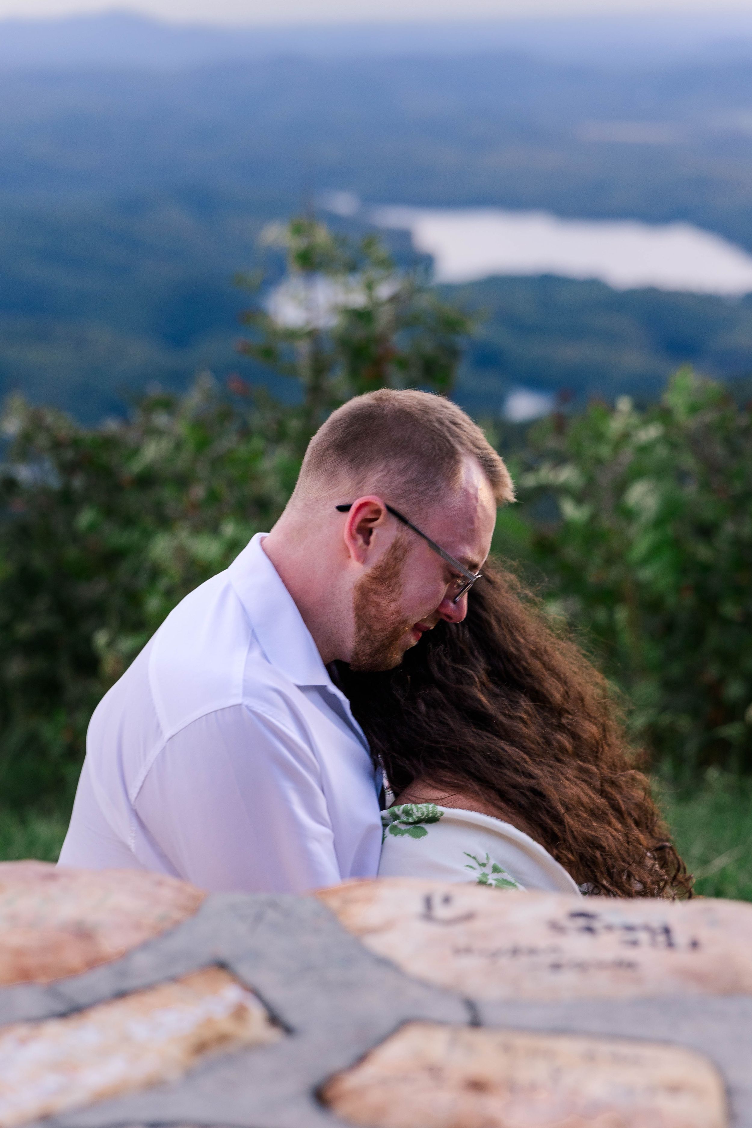 Couple shares intimate moment on mountain overlook with dramatic vista in background.