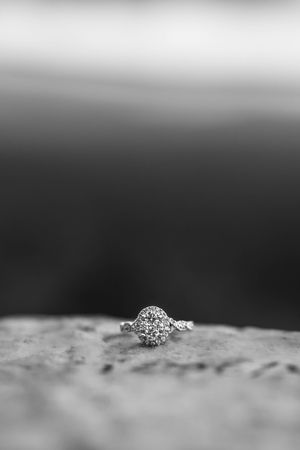 Black and white macro photograph of a diamond engagement ring sitting on textured stone.