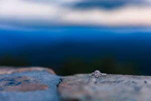 Diamond engagement ring placed on rocky surface with blue mountains in soft focus background.