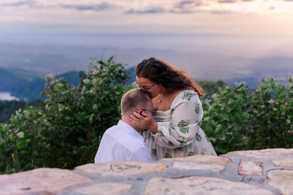 Intimate moment shared on mountain overlook with dramatic sunset sky and valley views.