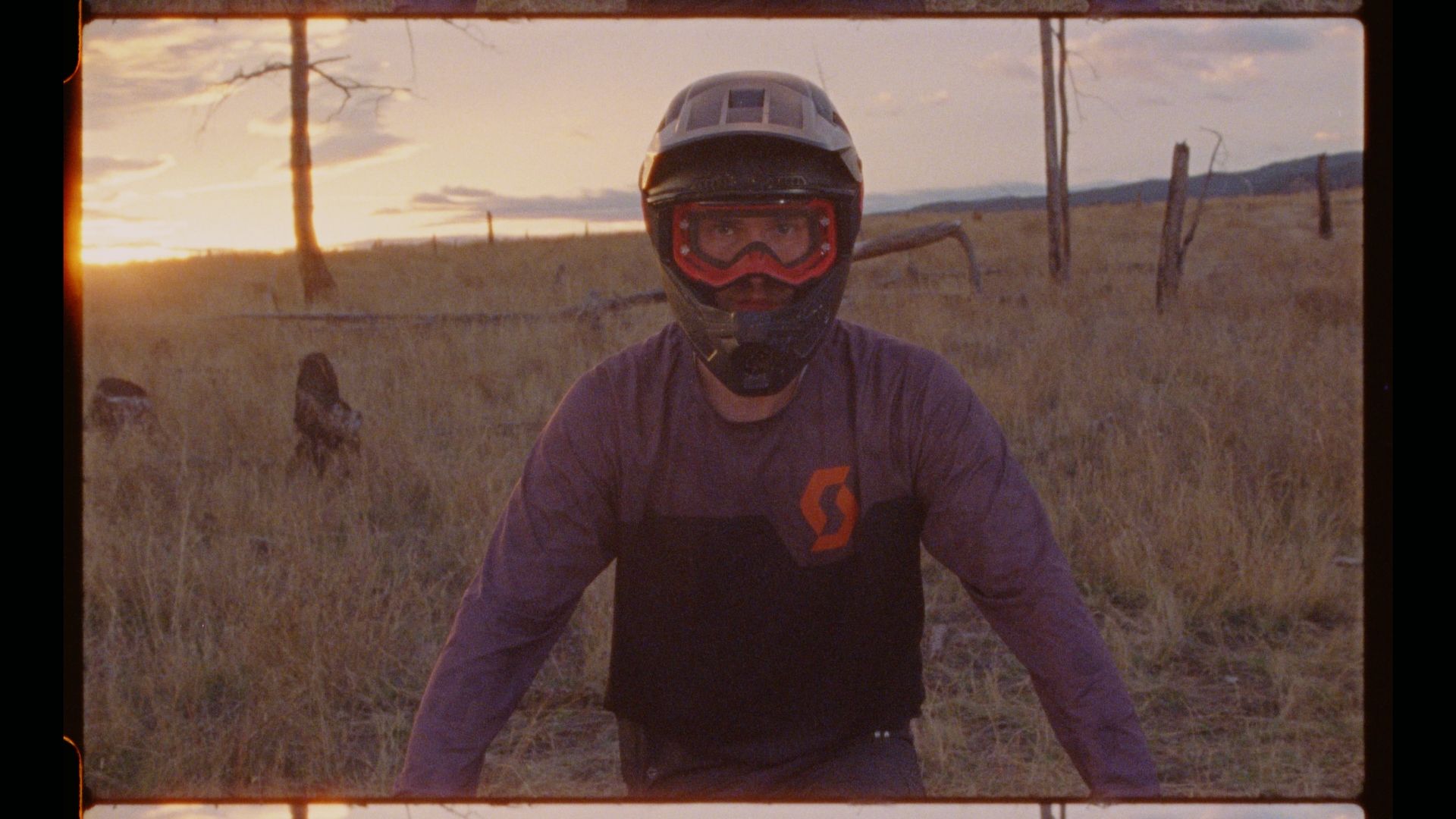 Mountain biker Joel Ducrot wearing protective gear poses in golden field at sunset.