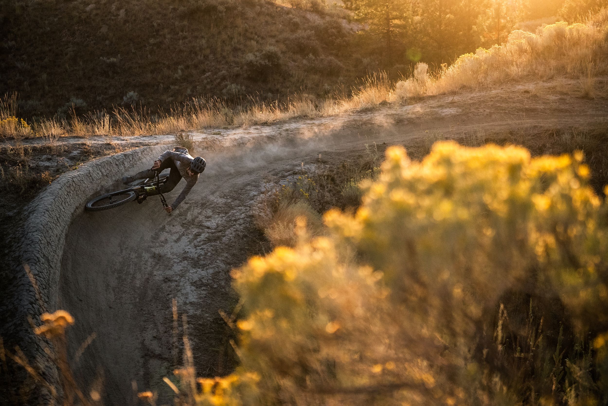 Mountain biker Joel Ducrot navigating a dusty trail curve at the Kamloops bike ranch during golden hour with sunlit brush in the background