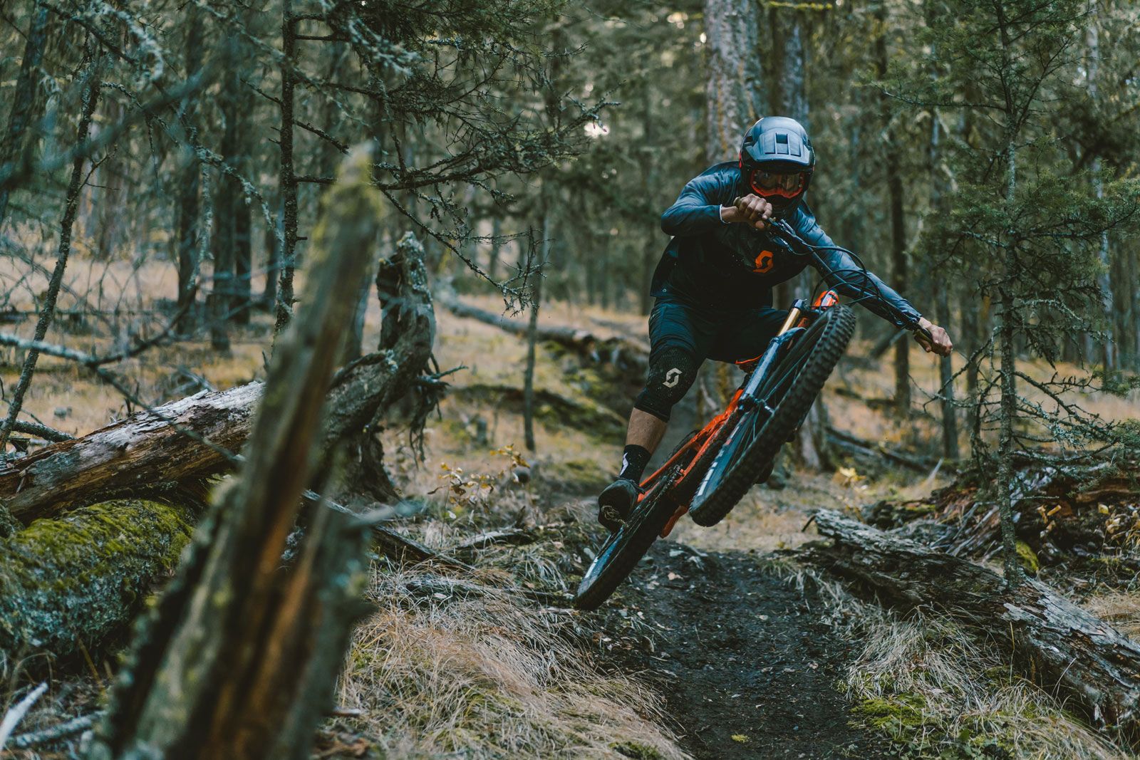 Mountain biker Joel Ducrot performing a turn on a rugged dirt trail through fallen trees. Shot by Steve Shannon