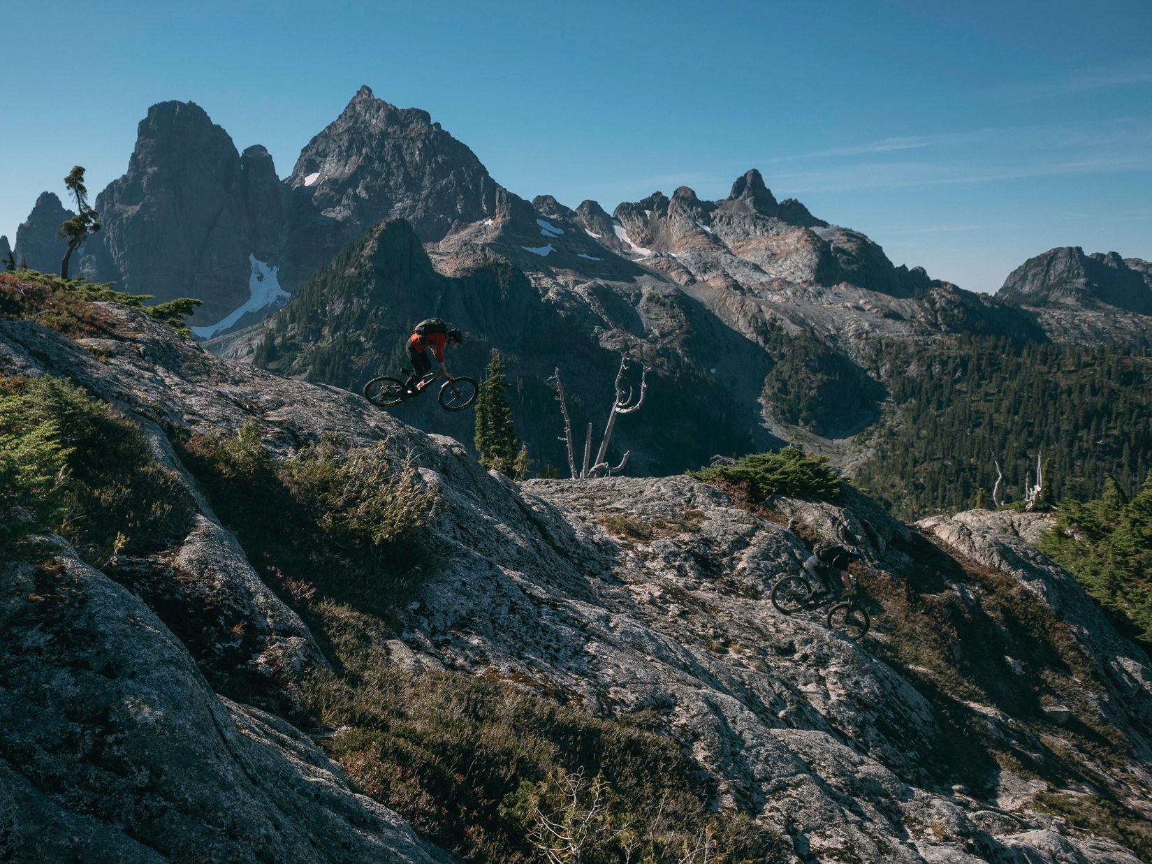 Mountain biker Joel Ducrot rides along rocky ridge with jagged peaks and blue skies in the background. Shot by Margus Riga