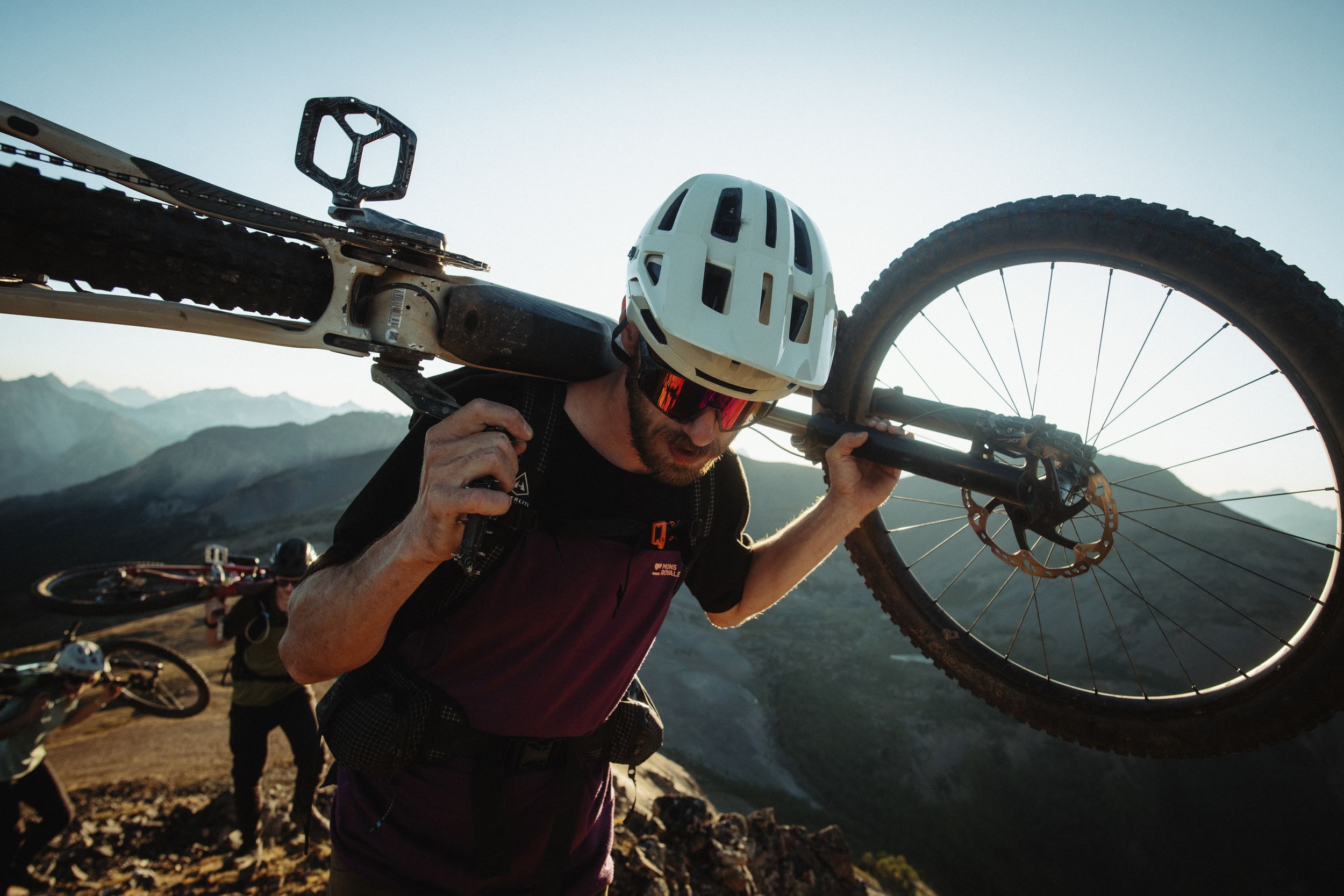 Mountain biker Joel Ducrot carrying bike on shoulders against mountainous backdrop. Shot by Margus Riga