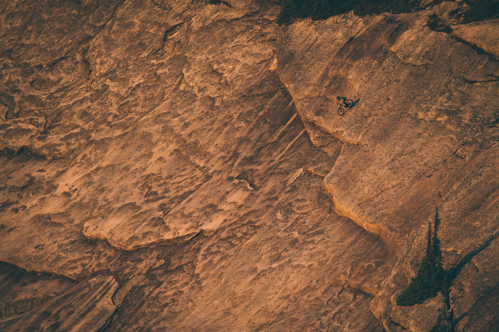 Mountain biker Joel Ducrot rides large rock face with deep grooves and natural patterns. Shot by Margus Riga