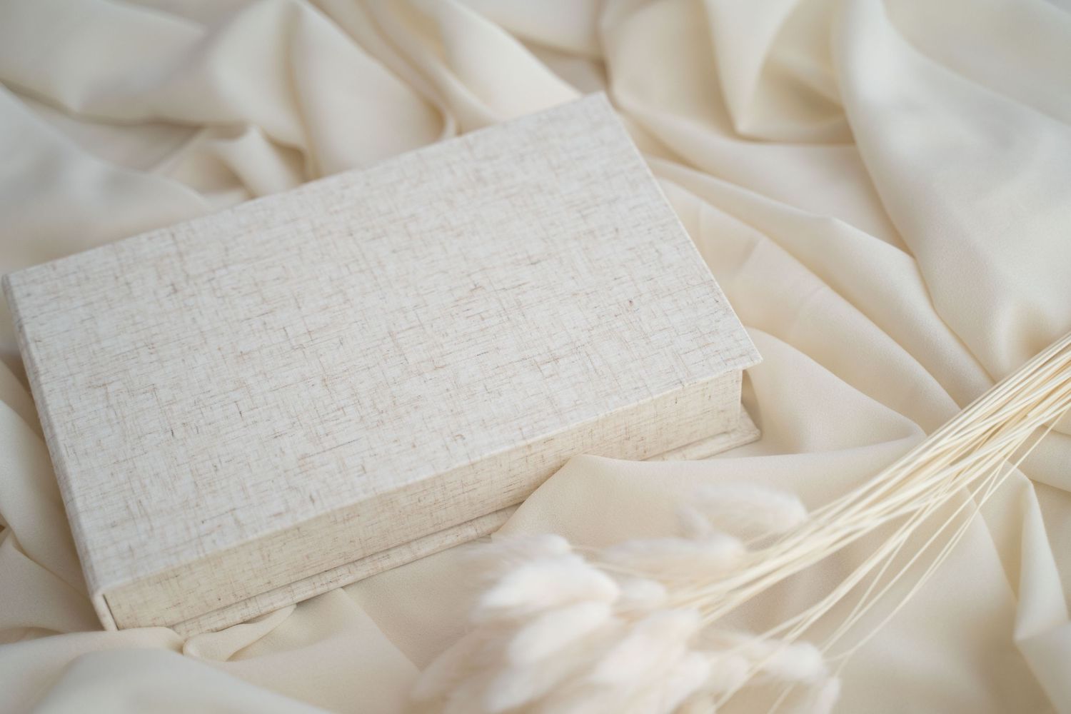 Blank white textured card on cream fabric with dried pampas grass, perfect for wedding stationery mockup.