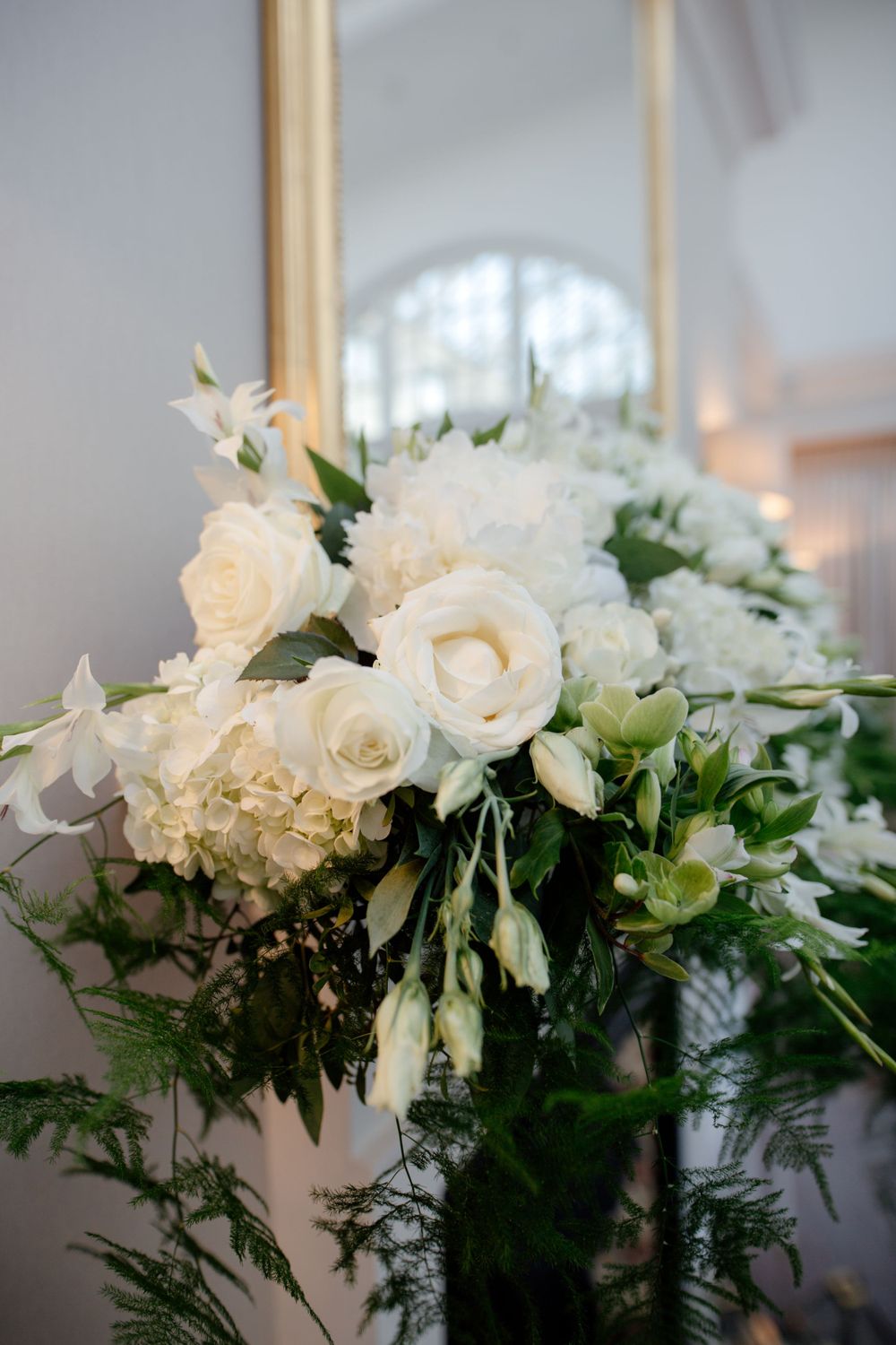 Elegant white floral wedding centerpiece arrangement with roses, hydrangeas and mixed greenery in soft lighting.