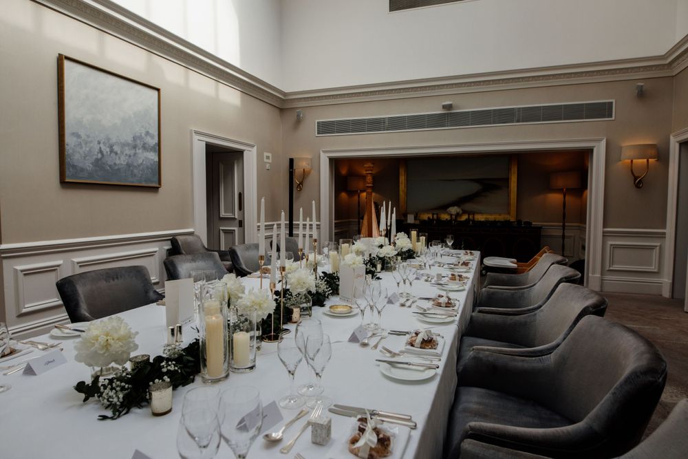 Elegantly set formal dining table with white flowers, candles and gray upholstered chairs in luxurious private room.