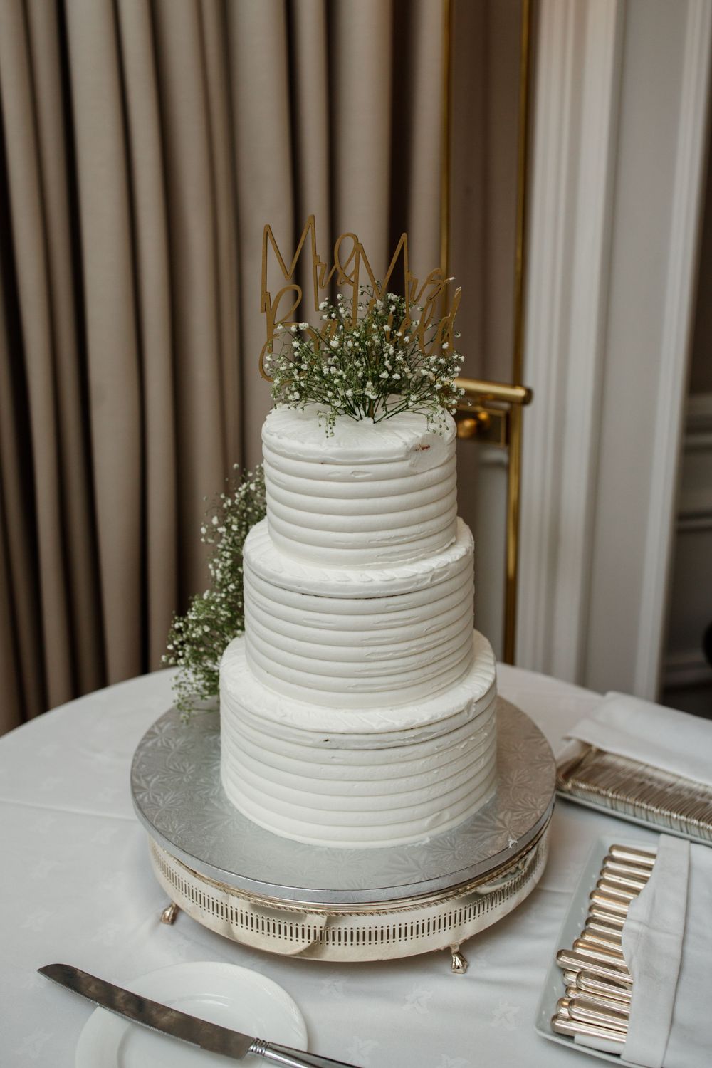Three-tiered white wedding cake with textured frosting and delicate baby's breath flowers on a silver cake stand.