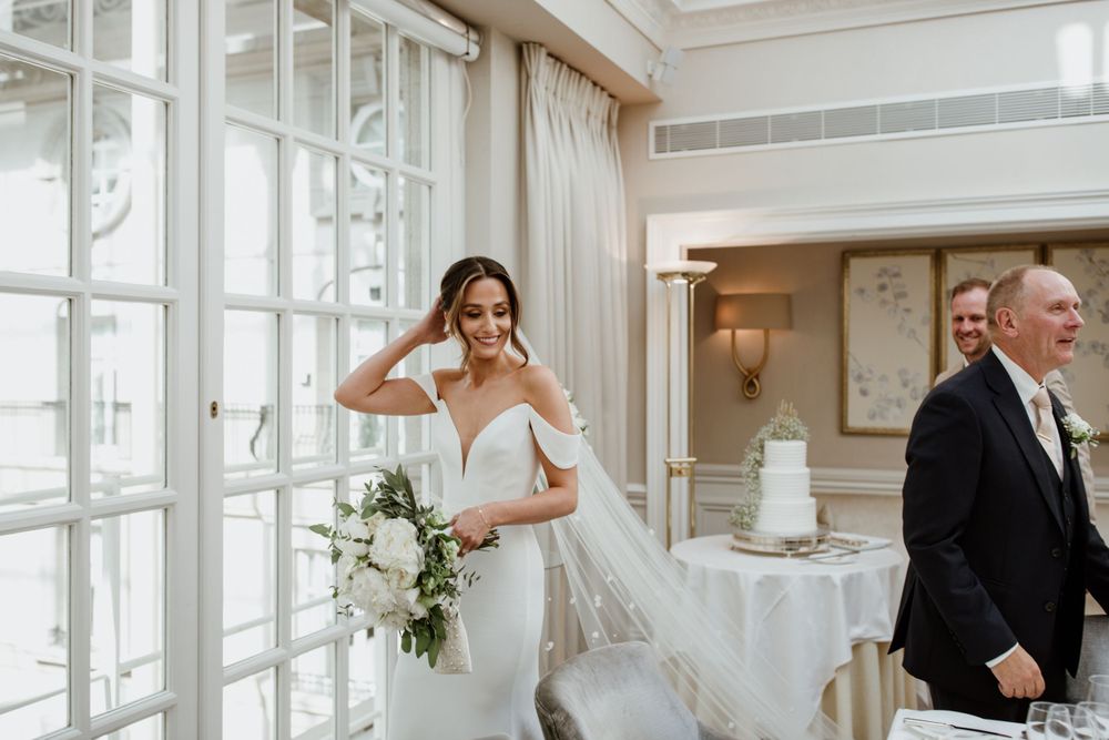 A joyful wedding moment captured at an elegant indoor venue with white decor and floral arrangements.