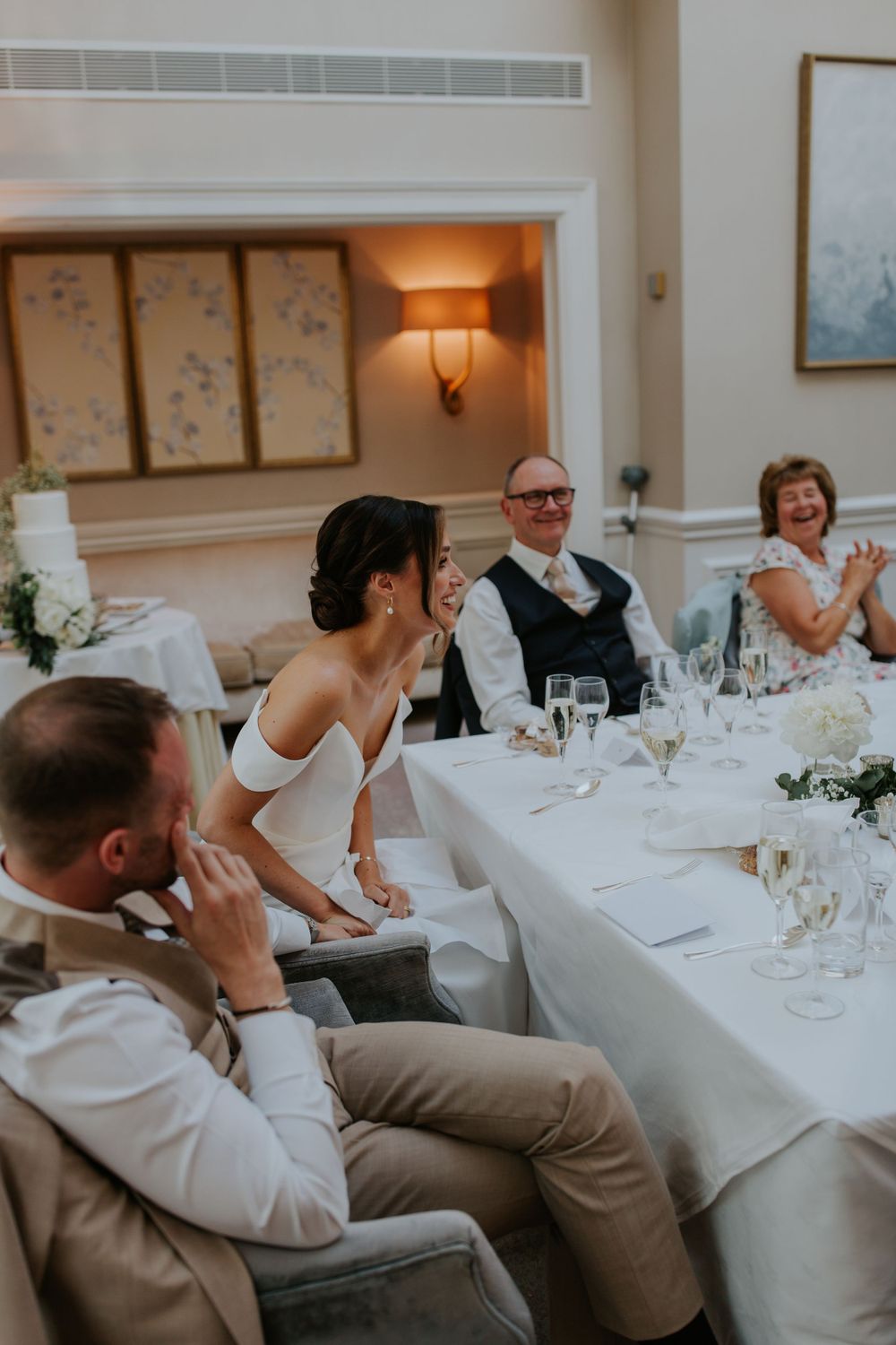 Guests seated at elegant wedding reception tables with white linens and floral centerpieces enjoying dinner conversation.
