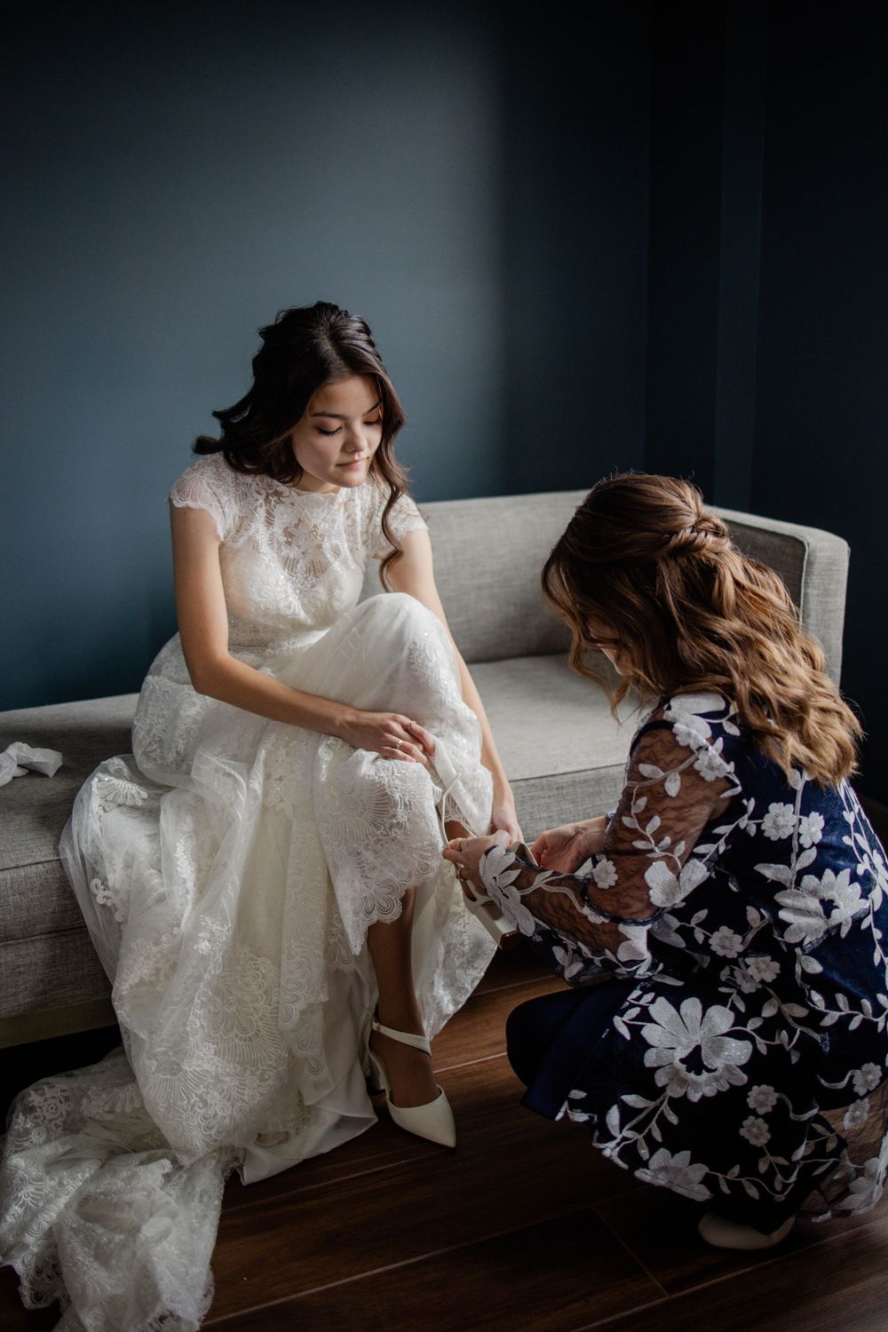 Final wedding dress preparations with intricate lace details against dark blue walls.
