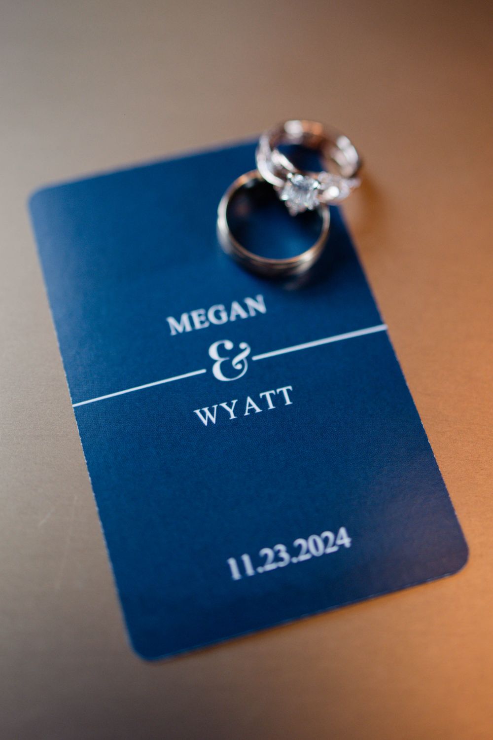 Wedding rings displayed on blue save-the-date card showing date and names Megan & Wyatt.