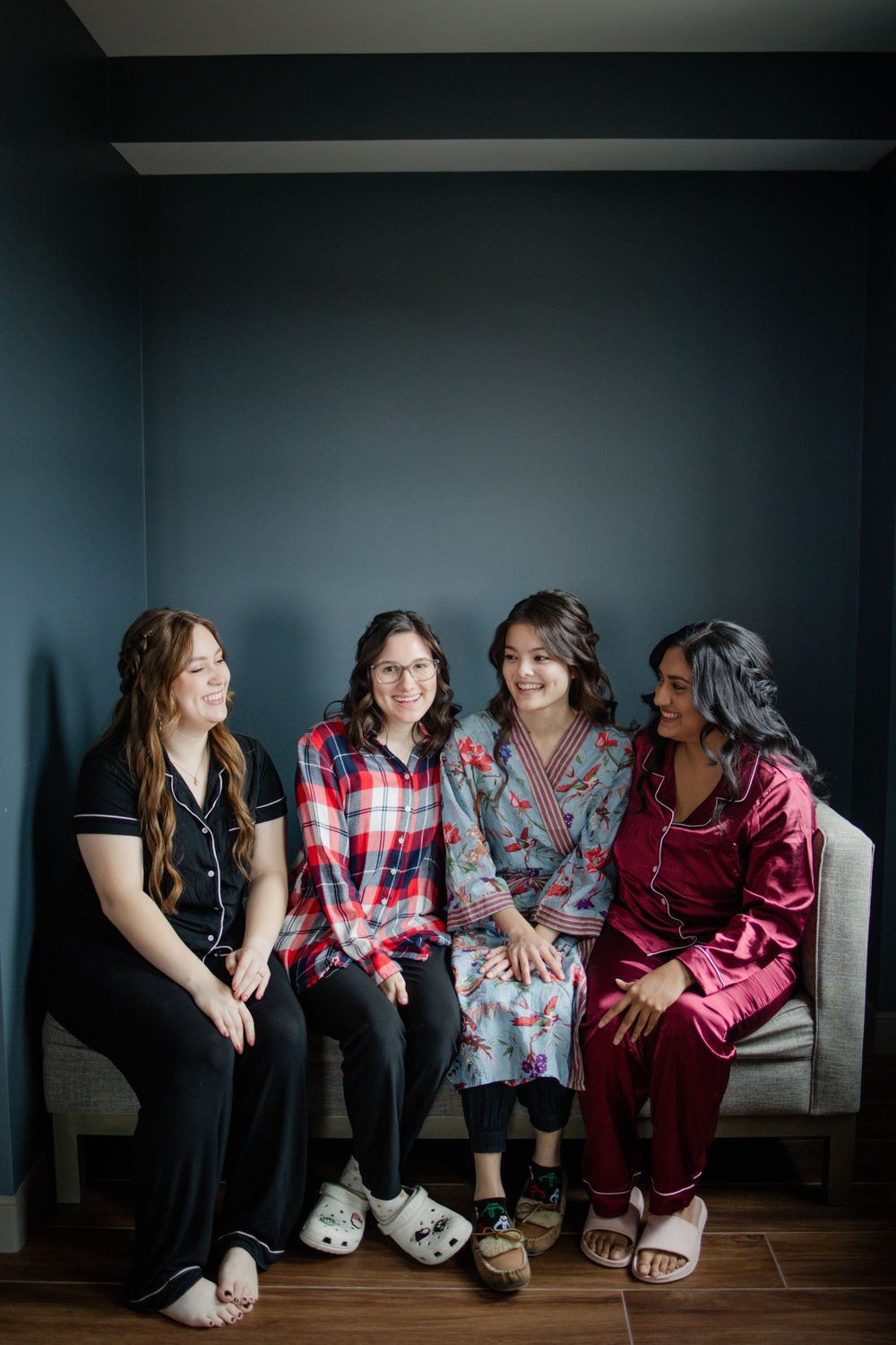 Four friends in sleepwear sitting together on white couch against dark wall.