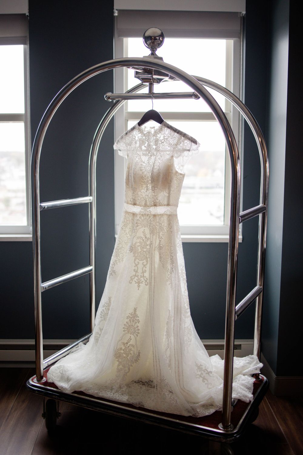 Elegant lace wedding dress displayed on silver circular garment rack against dark wall.