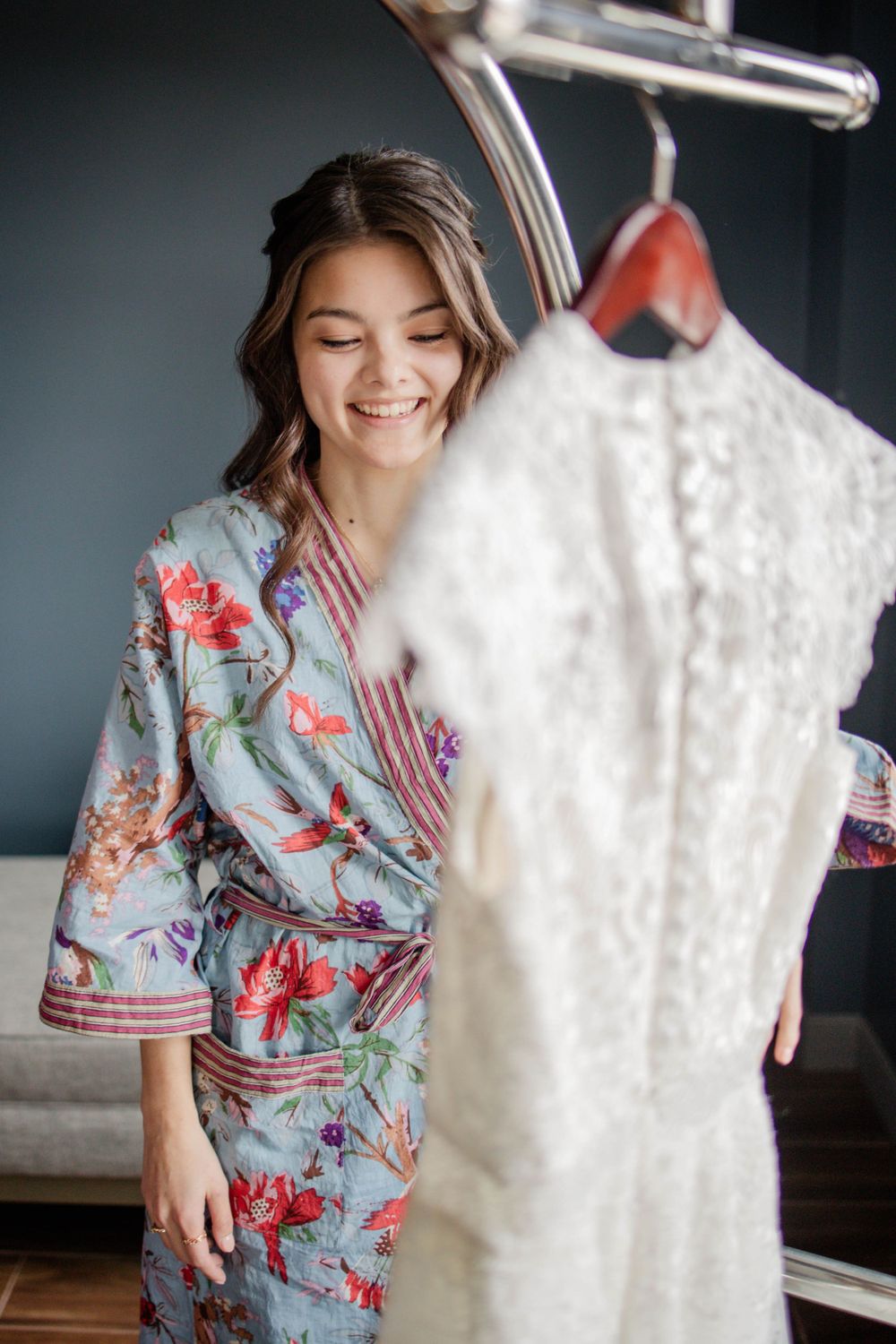 Woman in floral robe admiring white lace wedding dress on display stand.