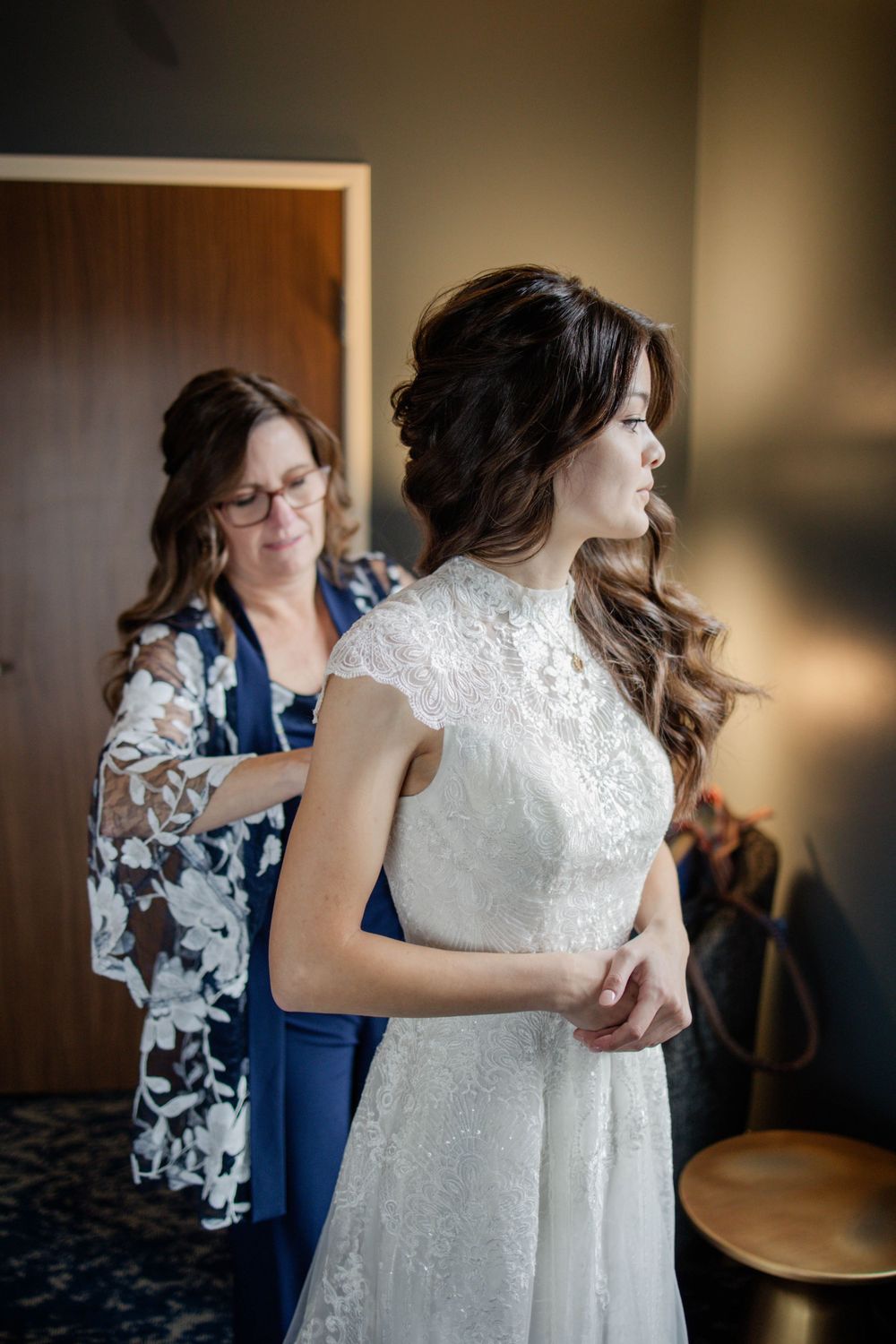 A wedding dress fitting shows delicate lace details as final adjustments are made in a softly lit room.