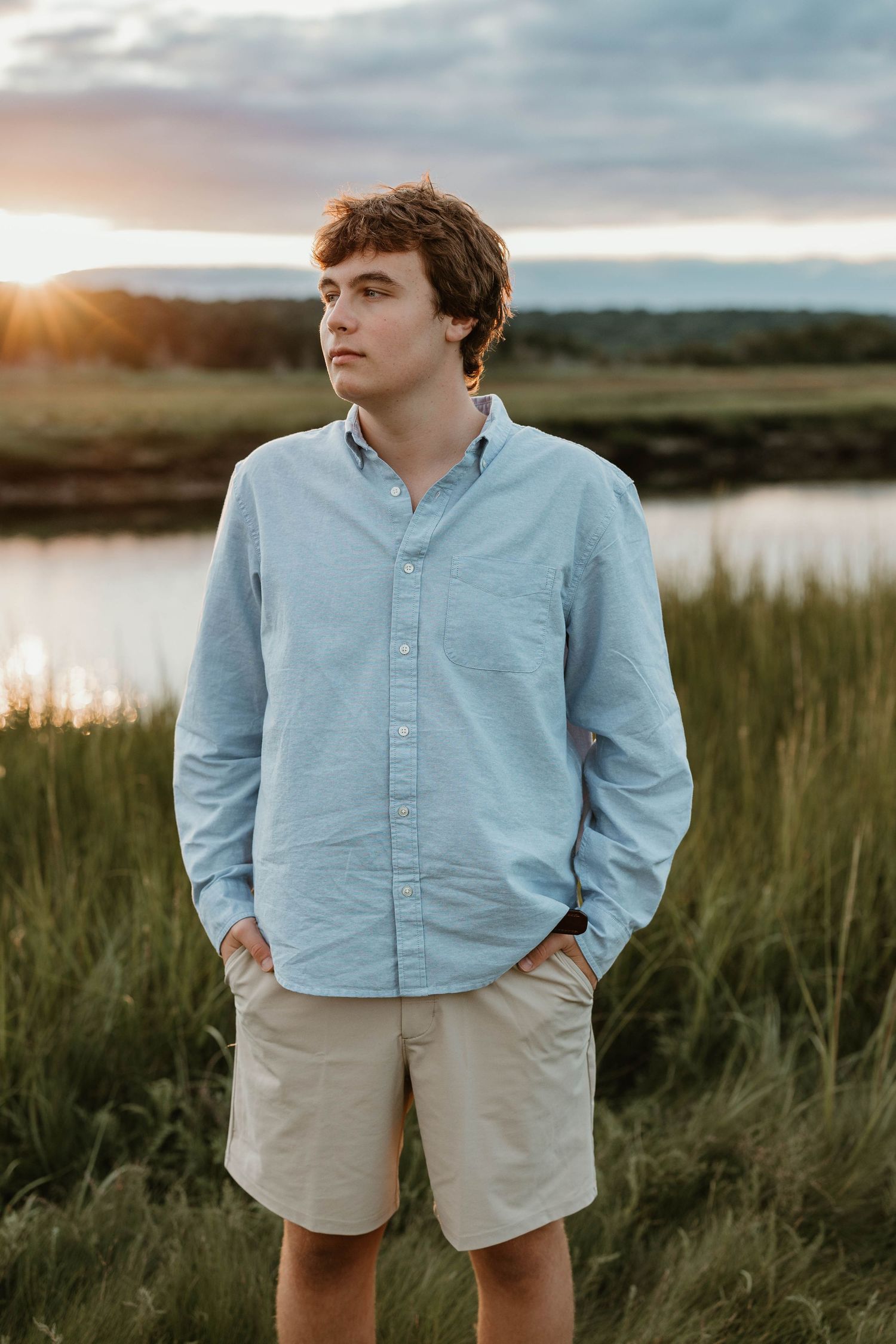 Person in light blue button-down shirt gazing at sunset over marsh landscape.