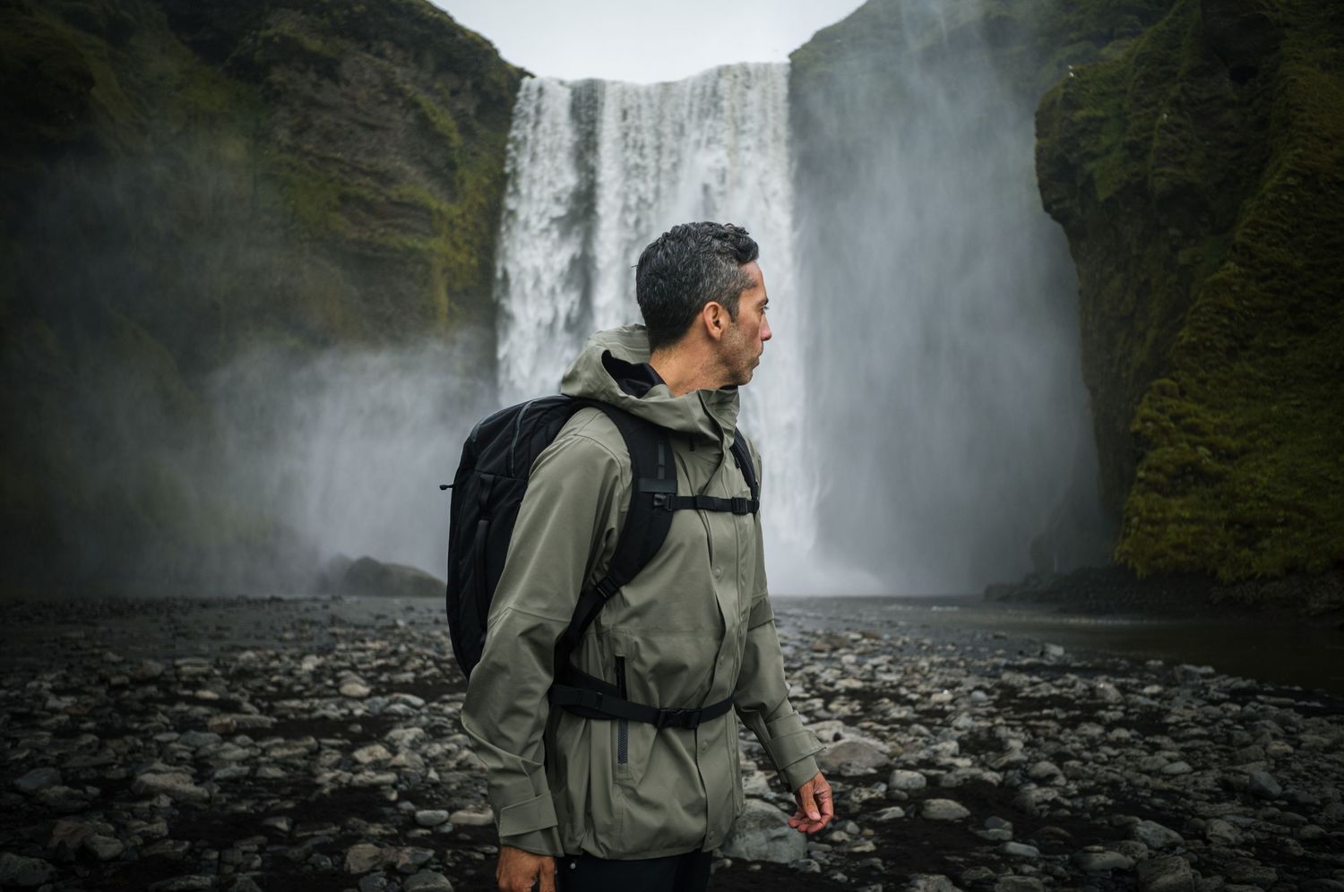 Adventure seeker standing at base of majestic waterfall in outdoor gear.