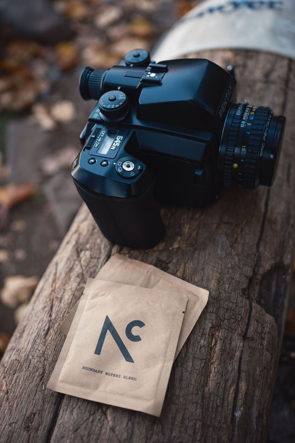 A black camera or optical device sits on a wooden surface next to a brown paper with a printed logo or symbol.