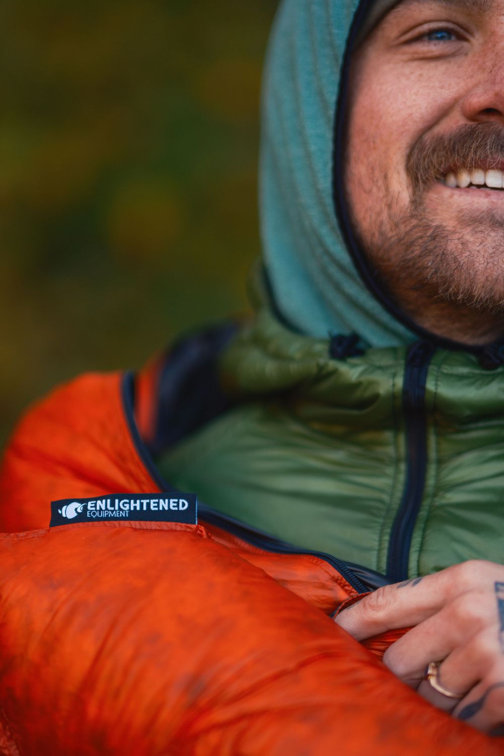 Close-up detail of orange and green outdoor jacket with Enlightened brand label.