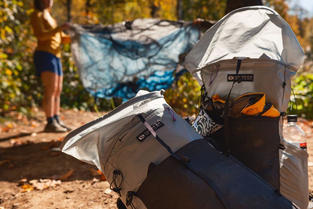 A collage of camping gear and outdoor equipment laid out on autumn leaves in a forest setting.