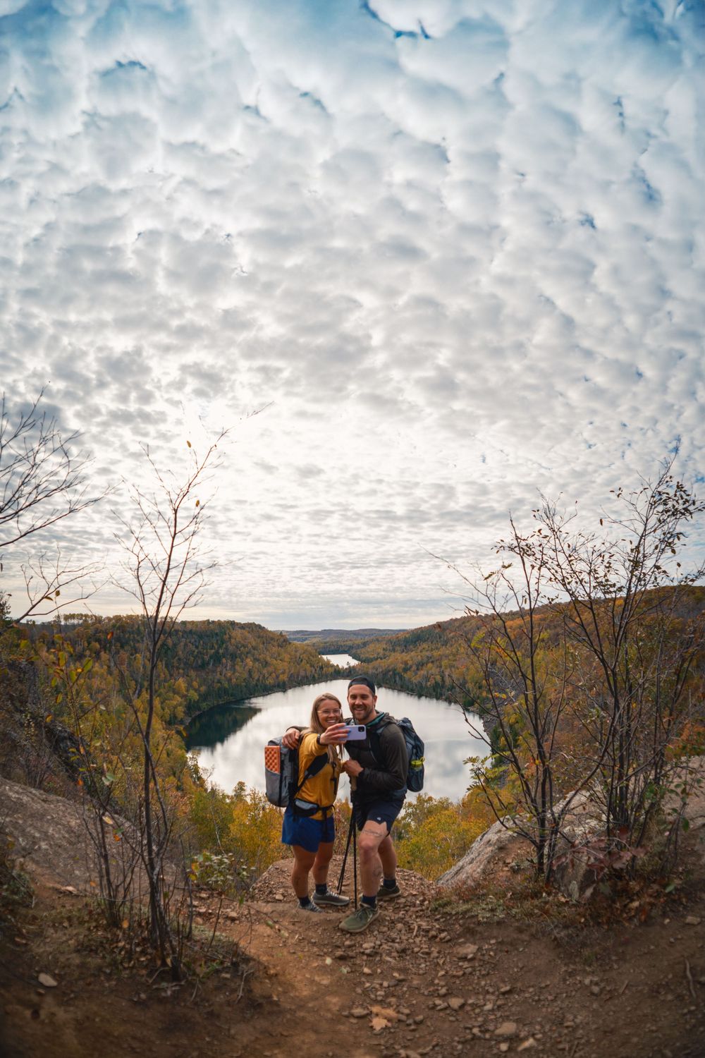 Hikers enjoying scenic mountain overlook with dramatic cloudy sky and fall foliage in background.