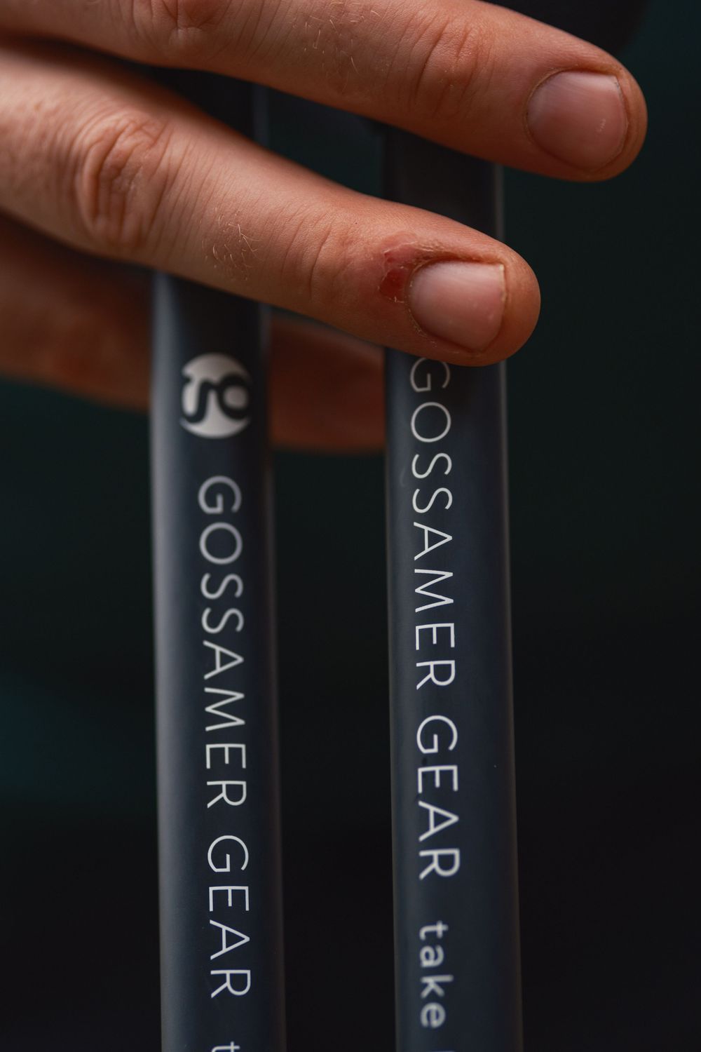 Close-up shot of fingers touching Gossamer Gear branded hiking poles against dark background.