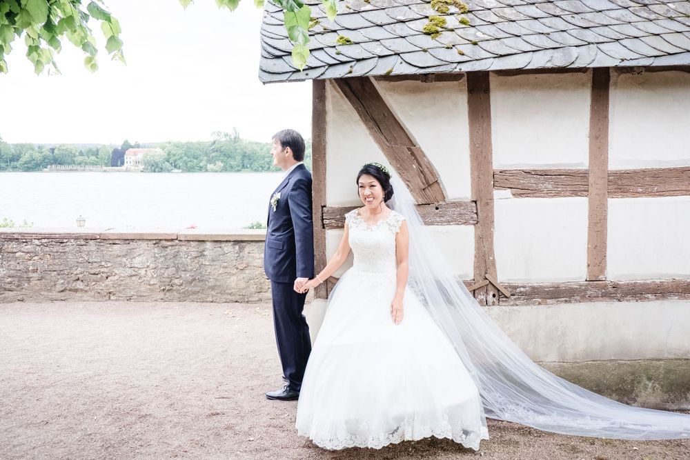 A wedding couple poses by a traditional half-timbered building with a lake view.