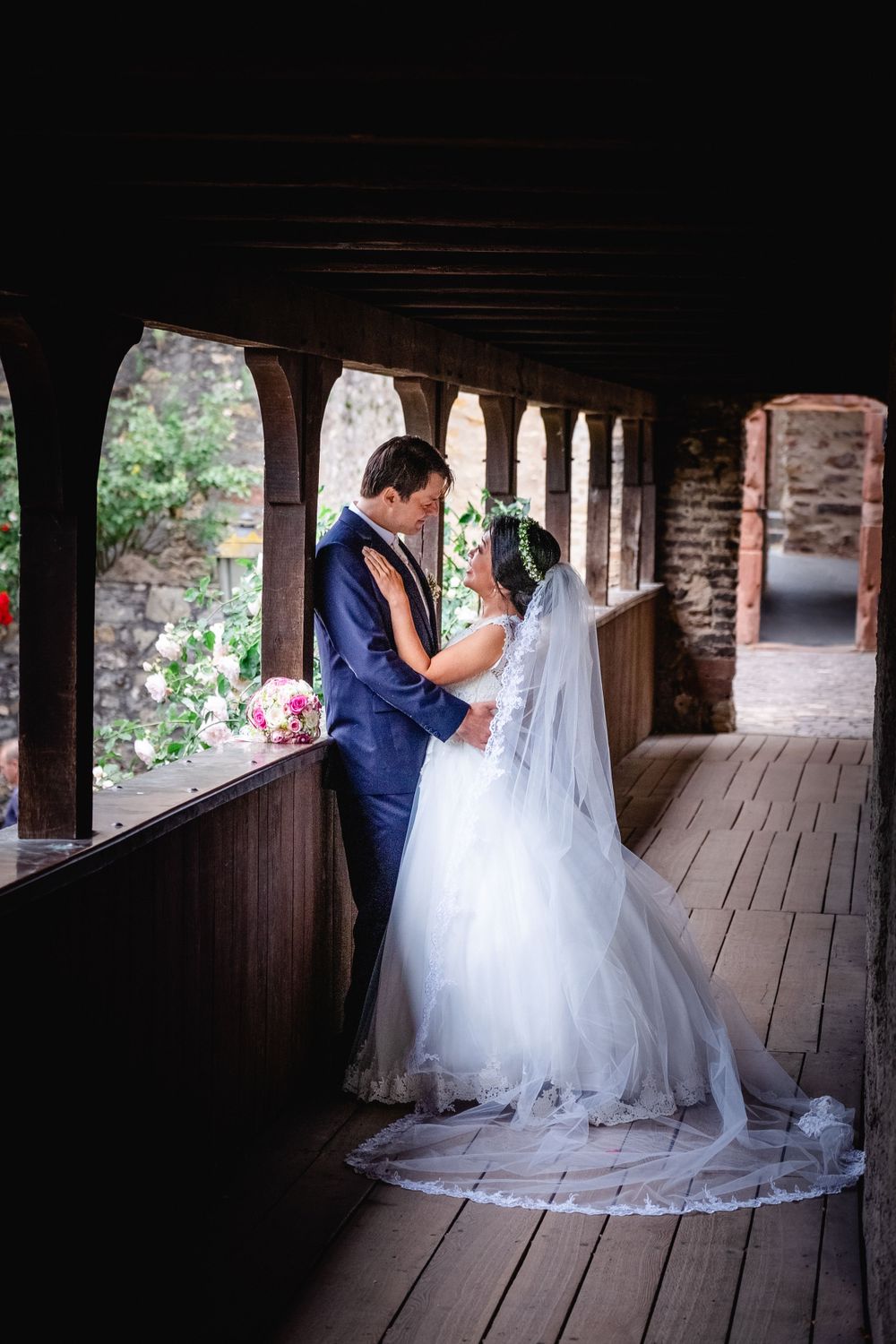 Wedding couple embracing under rustic wooden covered walkway with stone walls.