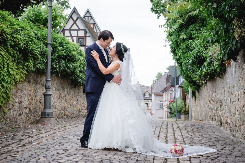 A romantic wedding couple embraces on a cobblestone street with traditional Tudor-style buildings in the background.