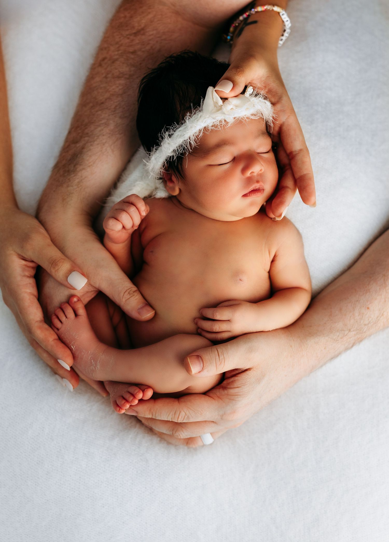 Sleeping newborn baby cradled in gentle hands with a delicate white feather resting near their head on white background. Rashinphotography