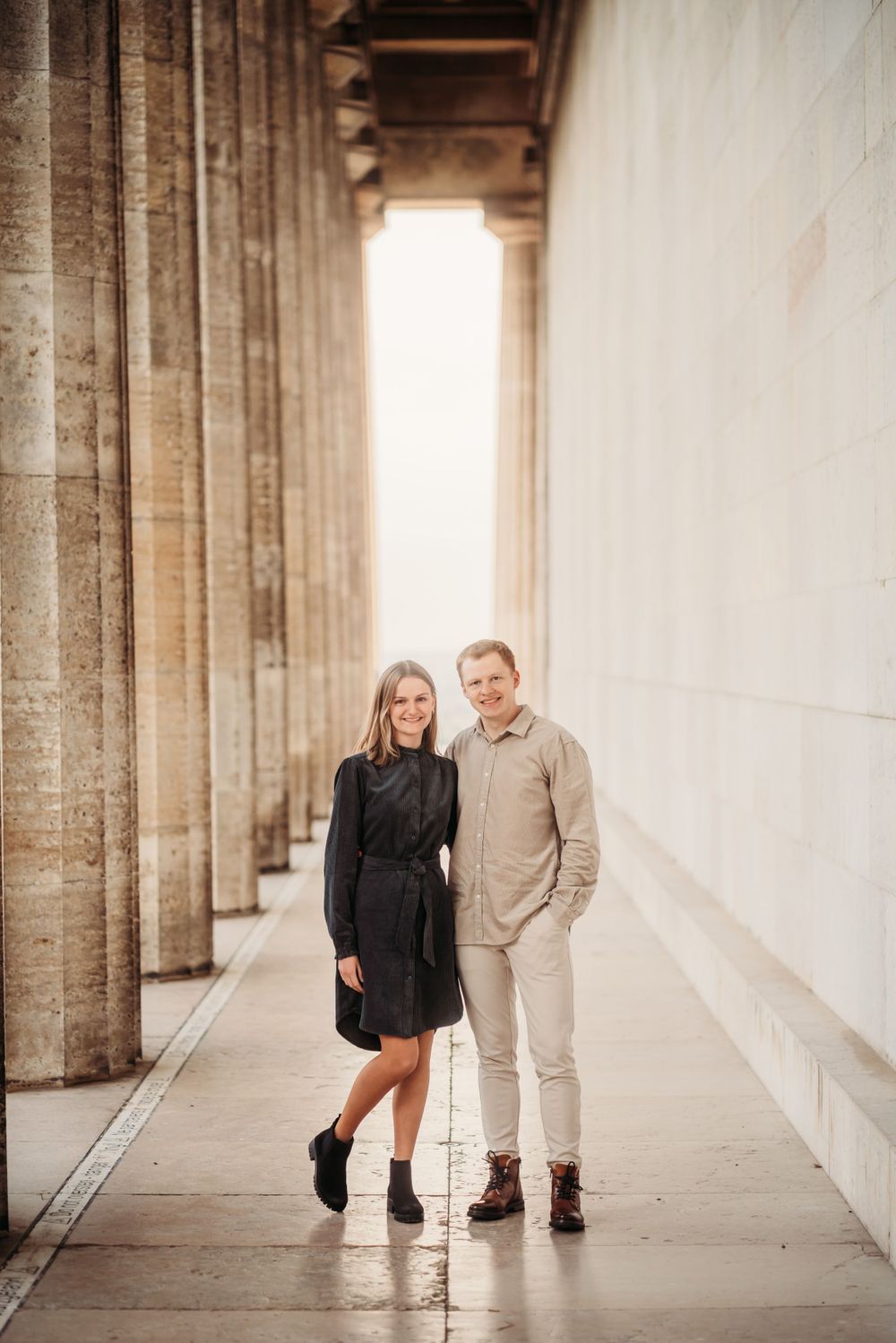 A stylish couple poses in a colonnade with dramatic lighting and architecture.