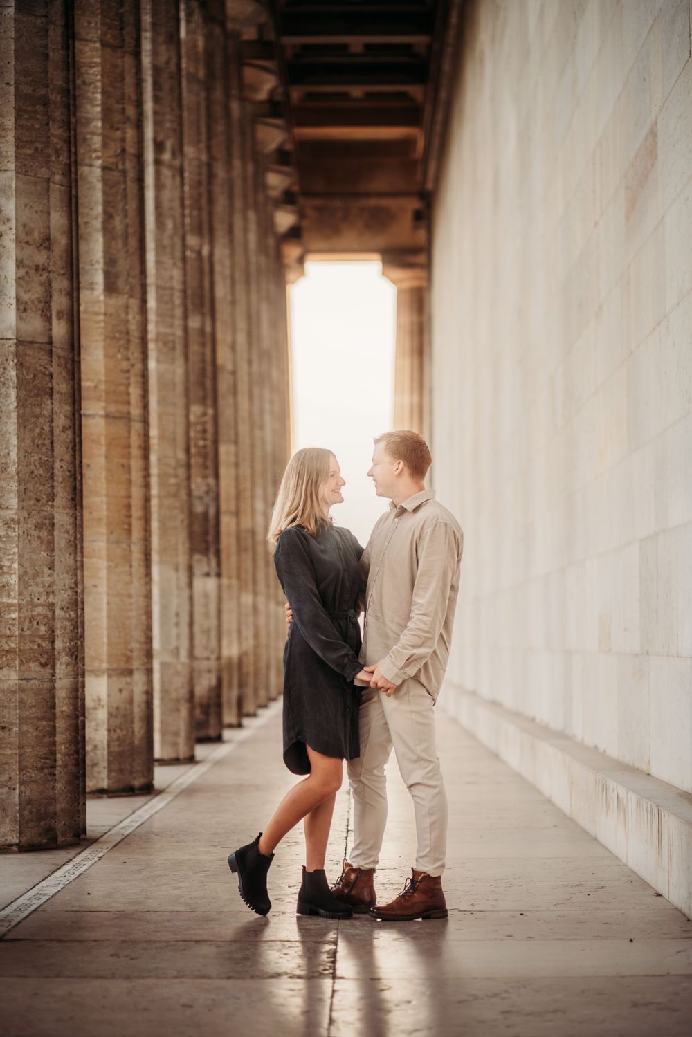A romantic couple embracing in a columned corridor with dramatic lighting and architecture.