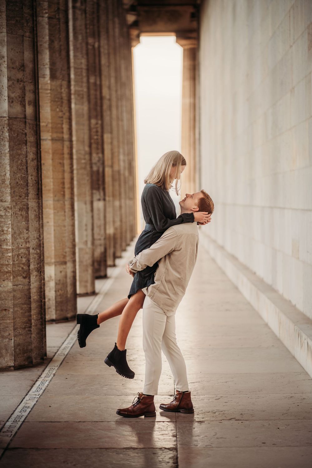 Couple sharing an intimate moment between stone pillars with warm backlighting.