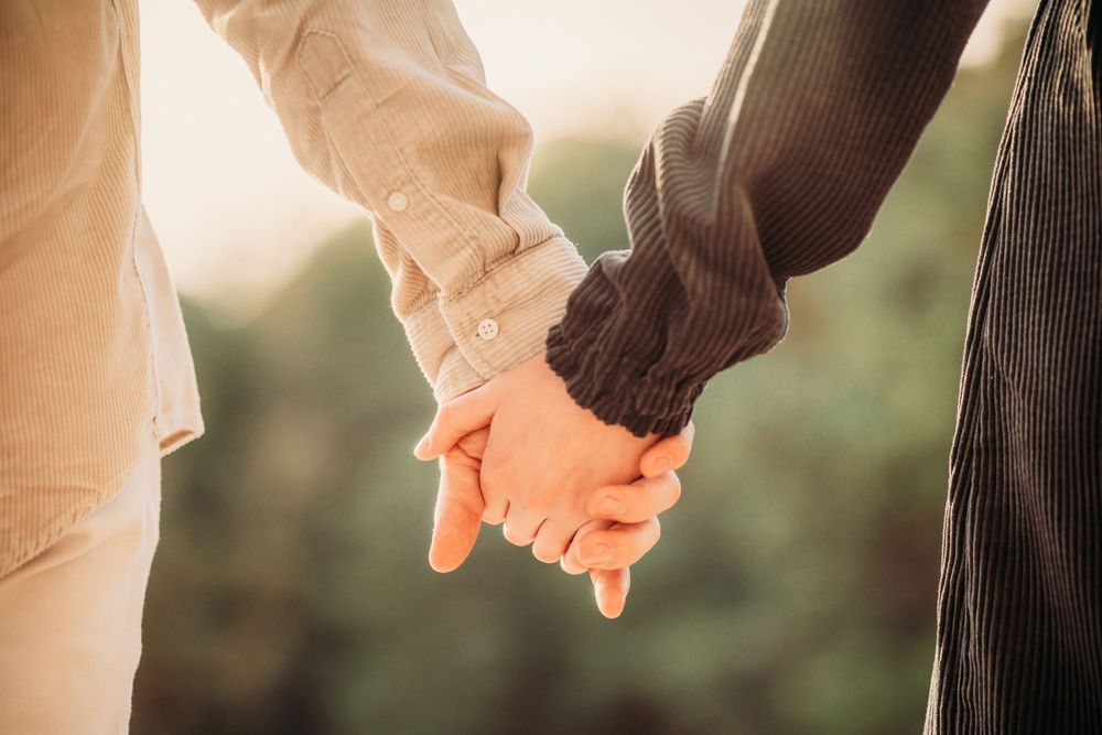 Close-up of two people holding hands tenderly in sunlit outdoor setting.