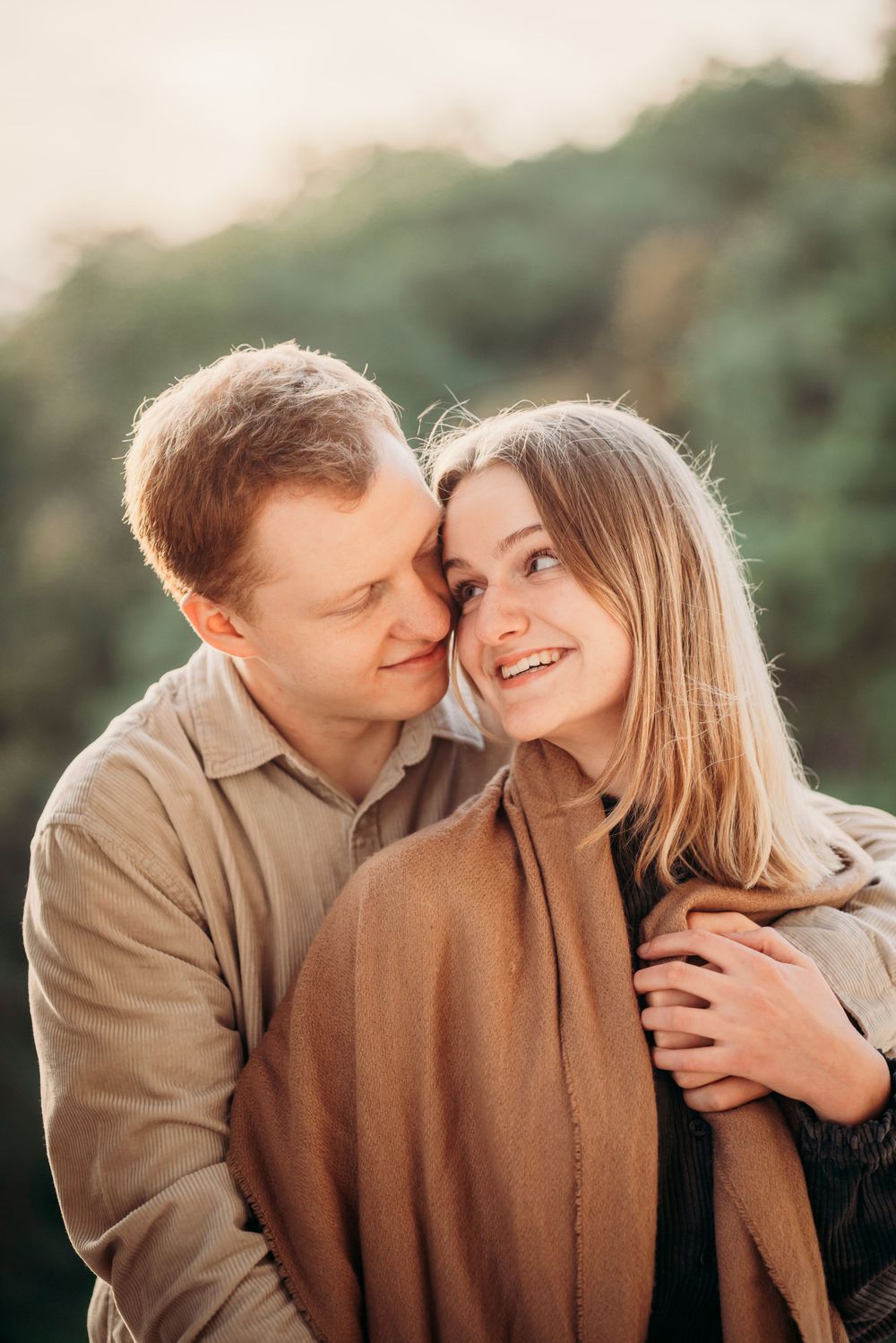 A tender moment between a couple wearing autumn colors against a blurred natural background.