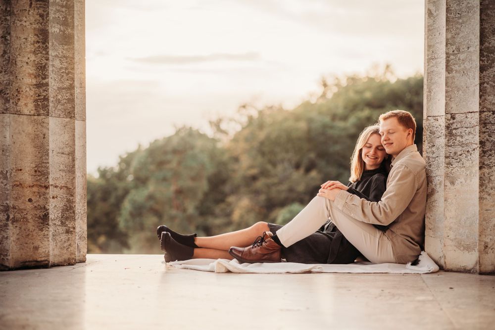 A couple relaxes on stone architecture floor with soft lighting and natural backdrop.