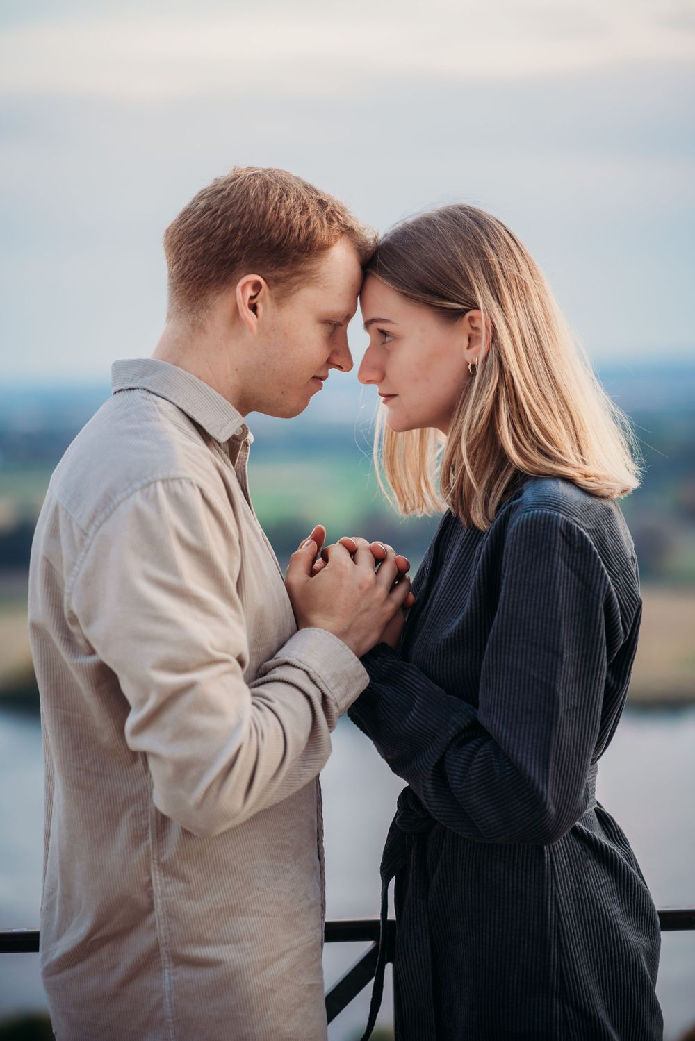 A couple shares an intimate moment while holding hands against a scenic overlook.