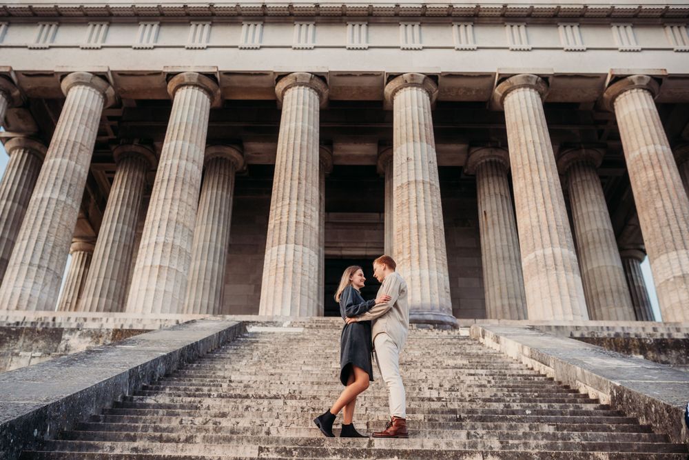 A couple embraces on the steps of a neoclassical building with grand columns.