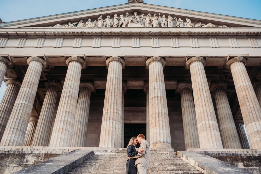 A couple embraces before a majestic Greek revival building with towering columns.
