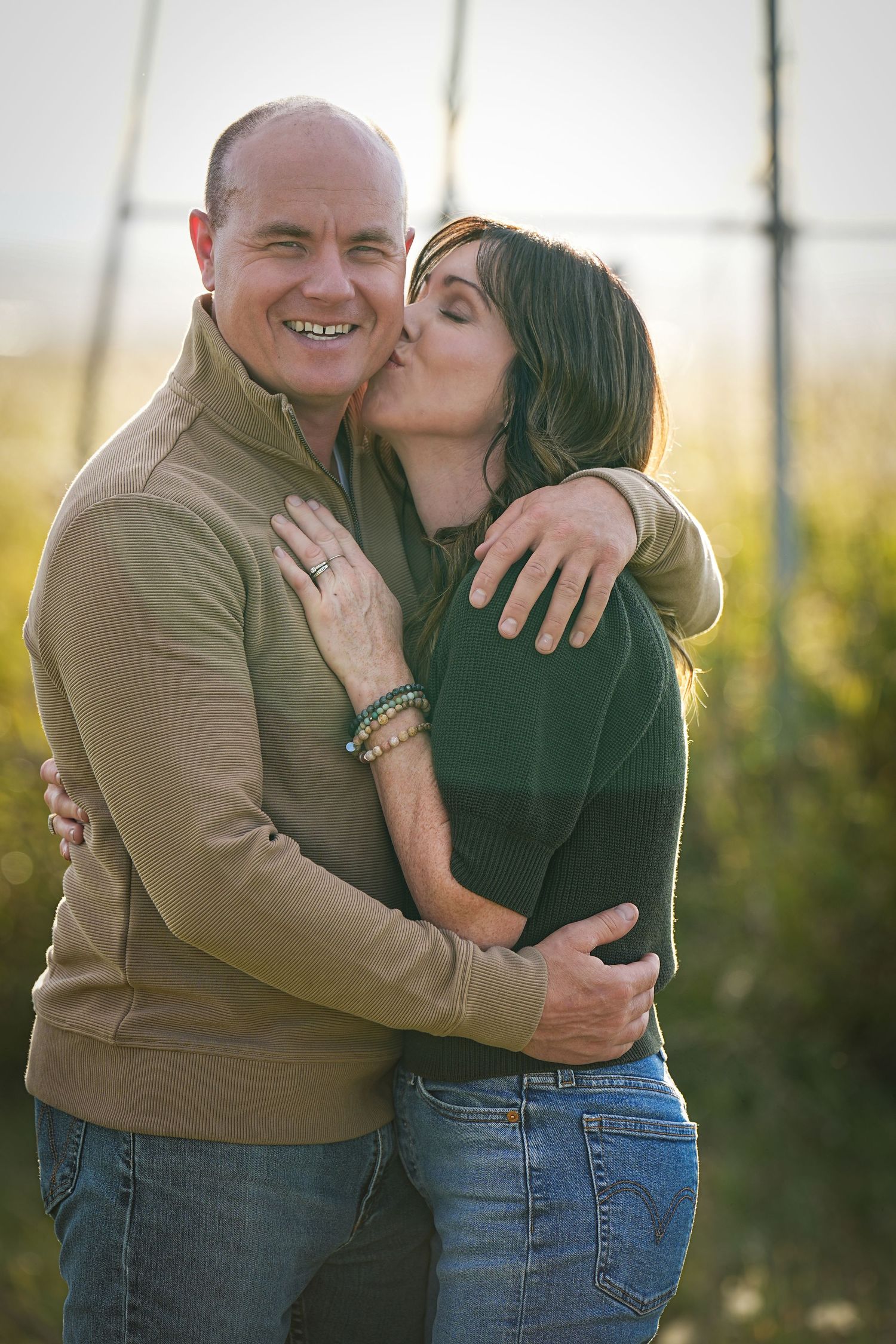 Affectionate couple embracing outdoors in casual clothing during golden hour.