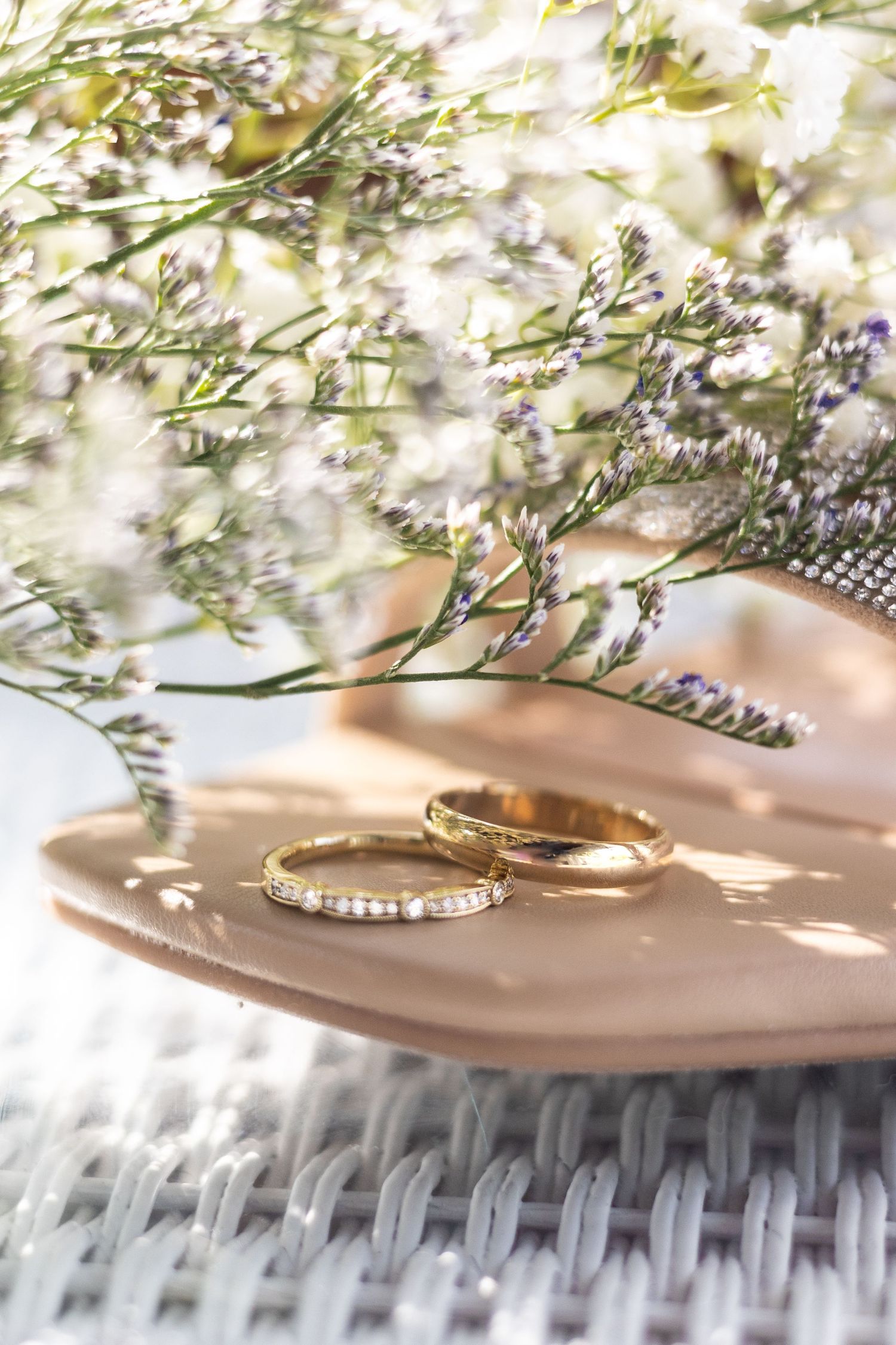 Two wedding rings on a pink dish with delicate white flowers and shadows creating a romantic, ethereal mood. West Michigan.