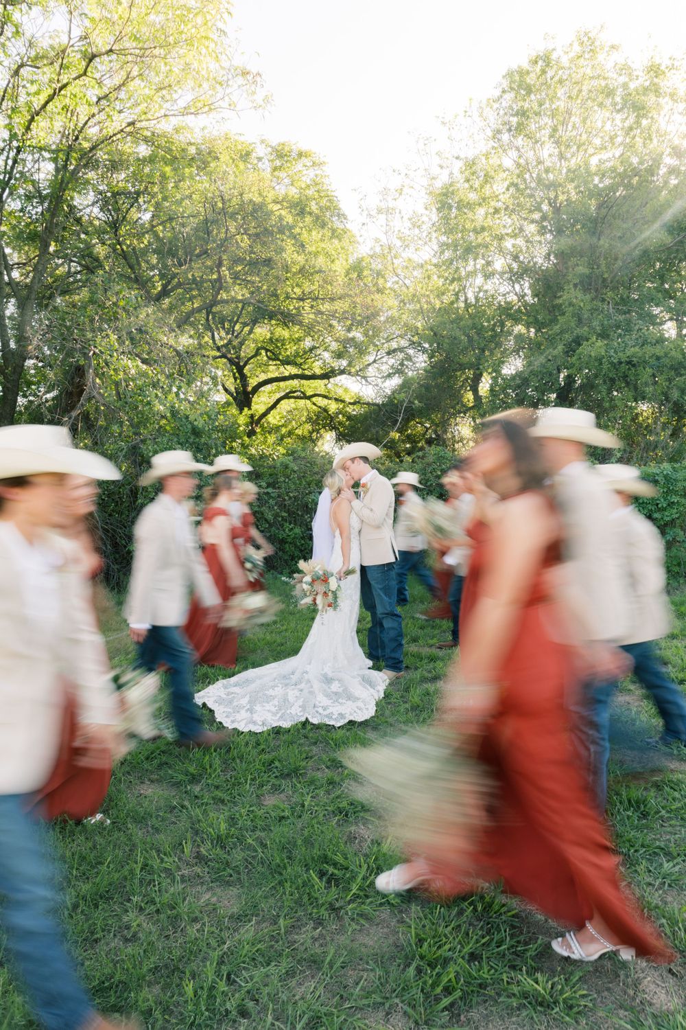 Motion blur captures wedding guests walking past couple during outdoor garden ceremony with lush greenery.